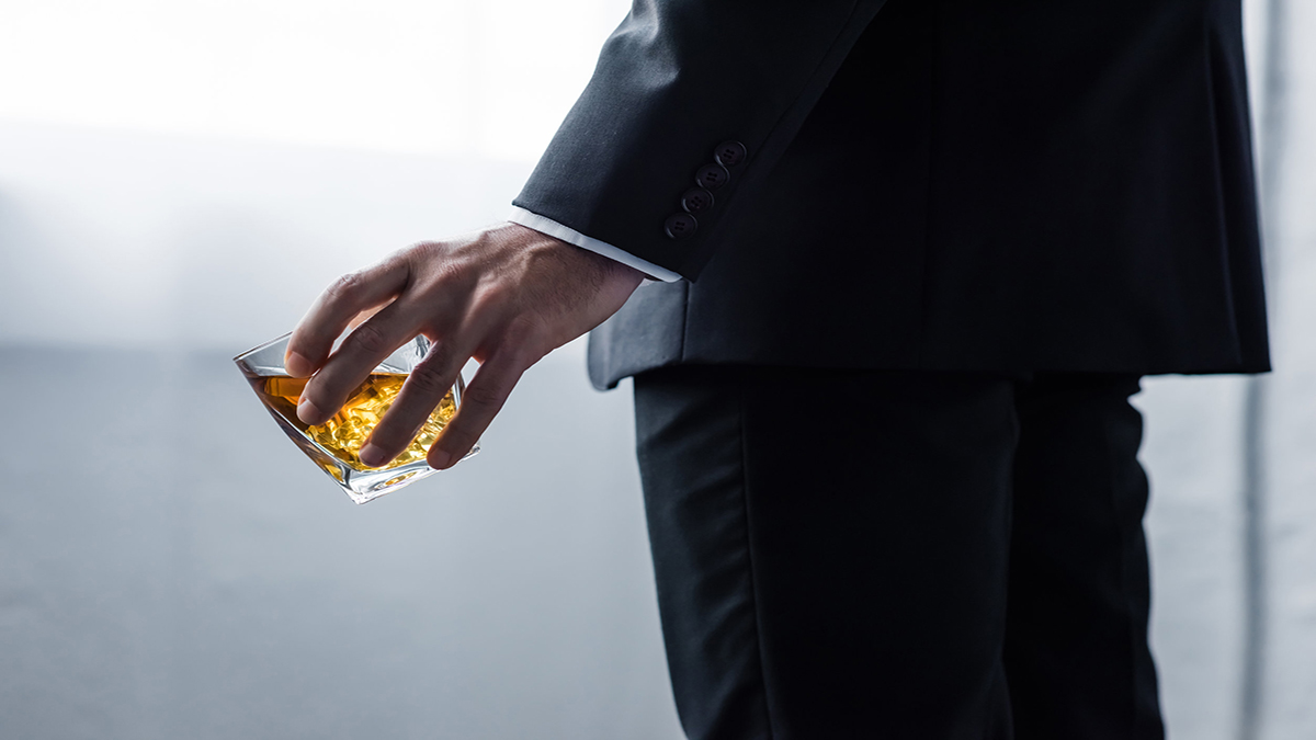 partial view of man in black suit holding glass of whiskey